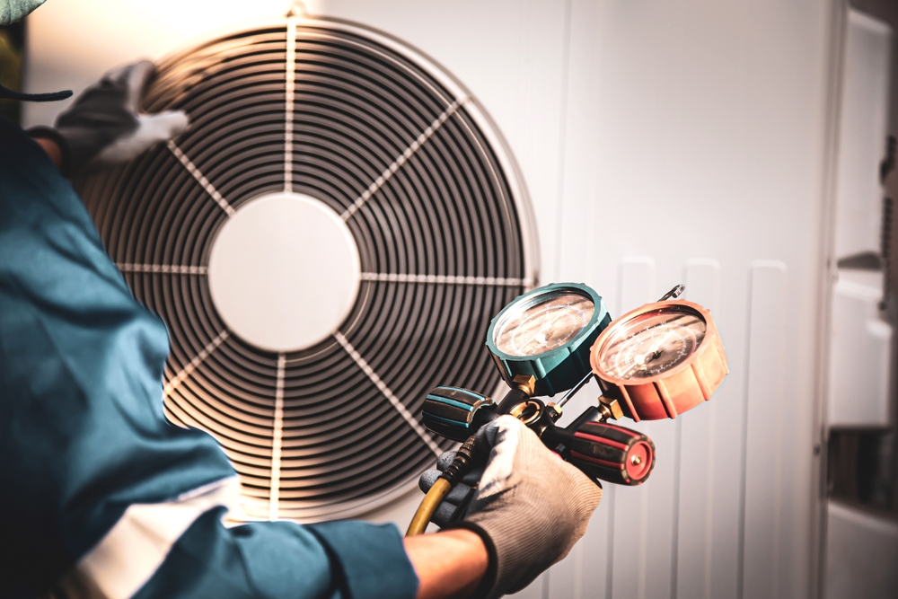 Technician holding pressure gauges beside outdoor HVAC equipment