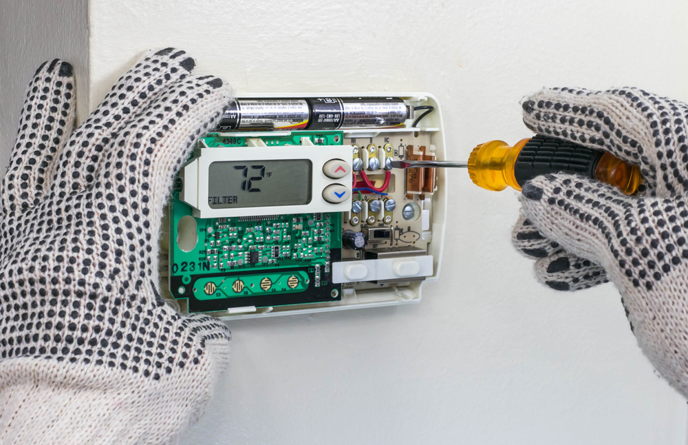 Gloved hands working on an open wall thermostat